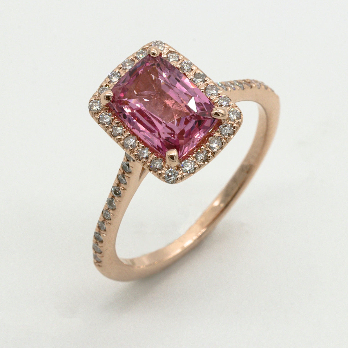 A rose gold ring with a rectangular pink gemstone surrounded by small diamonds